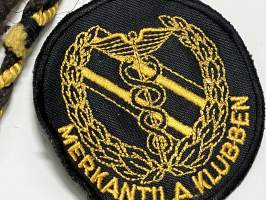 Merkantila klubben Åbo Akademi -erä sen toimintaan liittyviä yhden henkilön merkkejä; Ruusuke, kaulariipus, neulamerkit, mitali, kangasmerkit, tarra -osa hopeaa