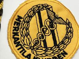 Merkantila klubben Åbo Akademi -erä sen toimintaan liittyviä yhden henkilön merkkejä; Ruusuke, kaulariipus, neulamerkit, mitali, kangasmerkit, tarra -osa hopeaa